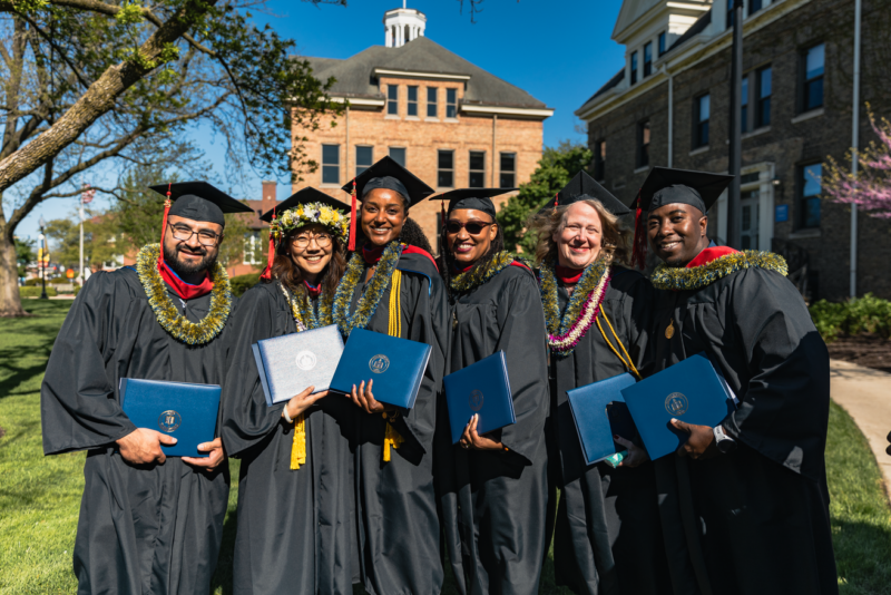 Students in graduation robes smiling and holding diplomas