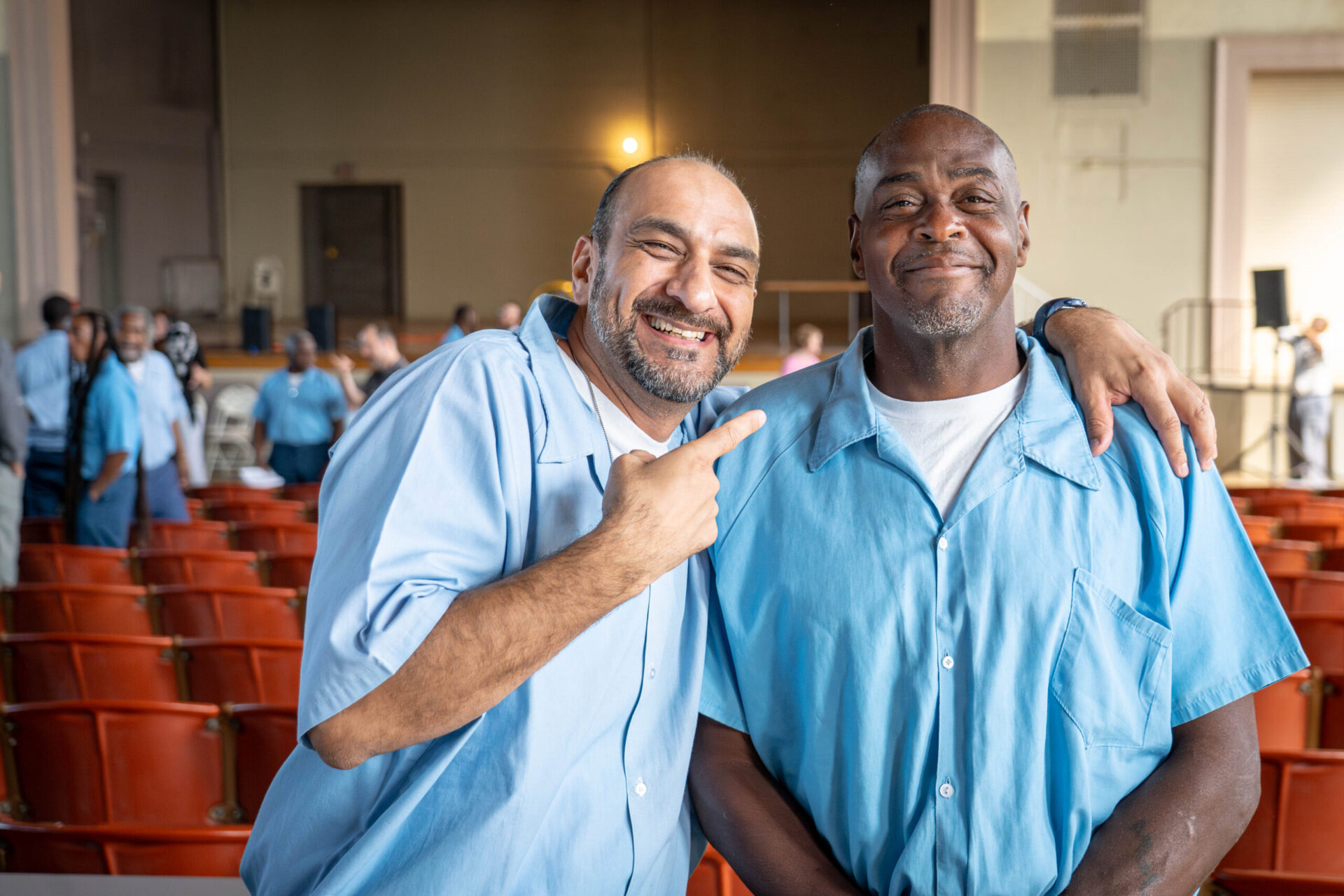Prisoner and student at Statesville correctional center wears blue prison uniform, smiling and pointing to his friend.