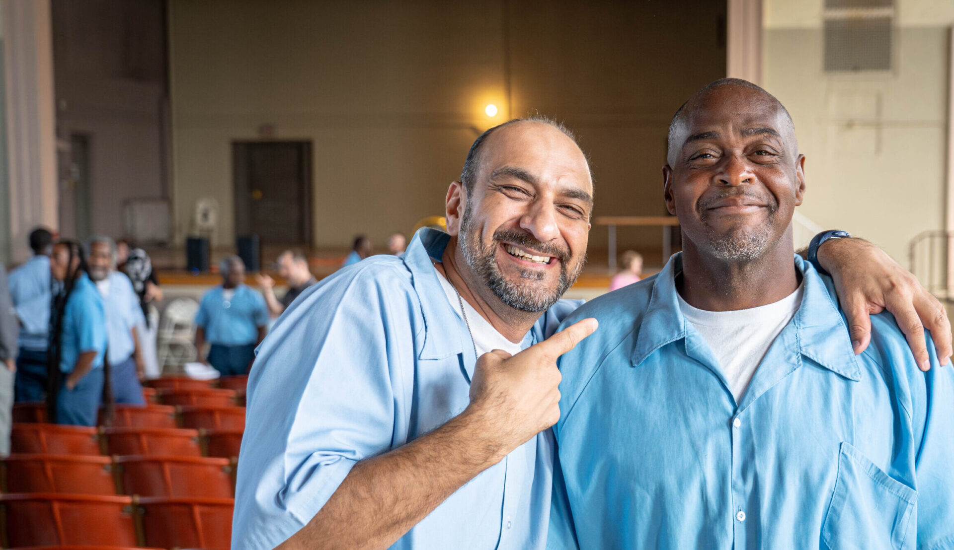 Prisoner and student at Statesville correctional center wears blue prison uniform, smiling and pointing to his friend.
