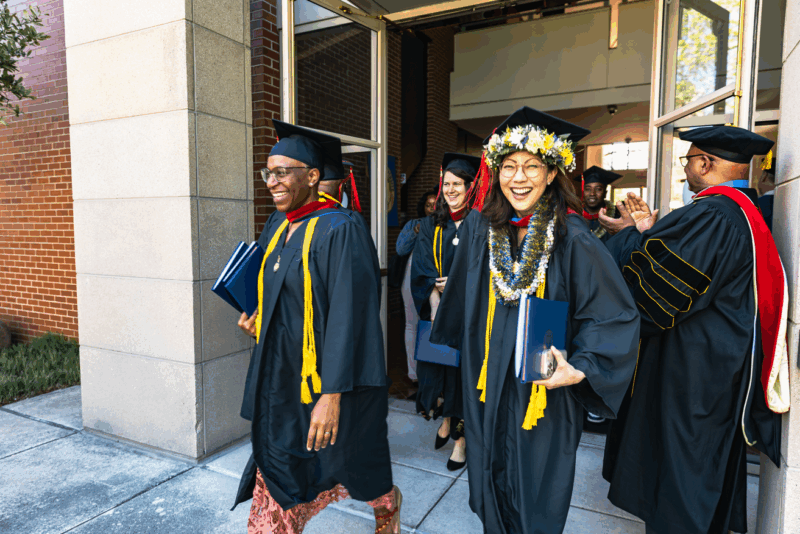 Seminary master's graduate walks out of 2025 commencement with full regalia and flowers around her cap