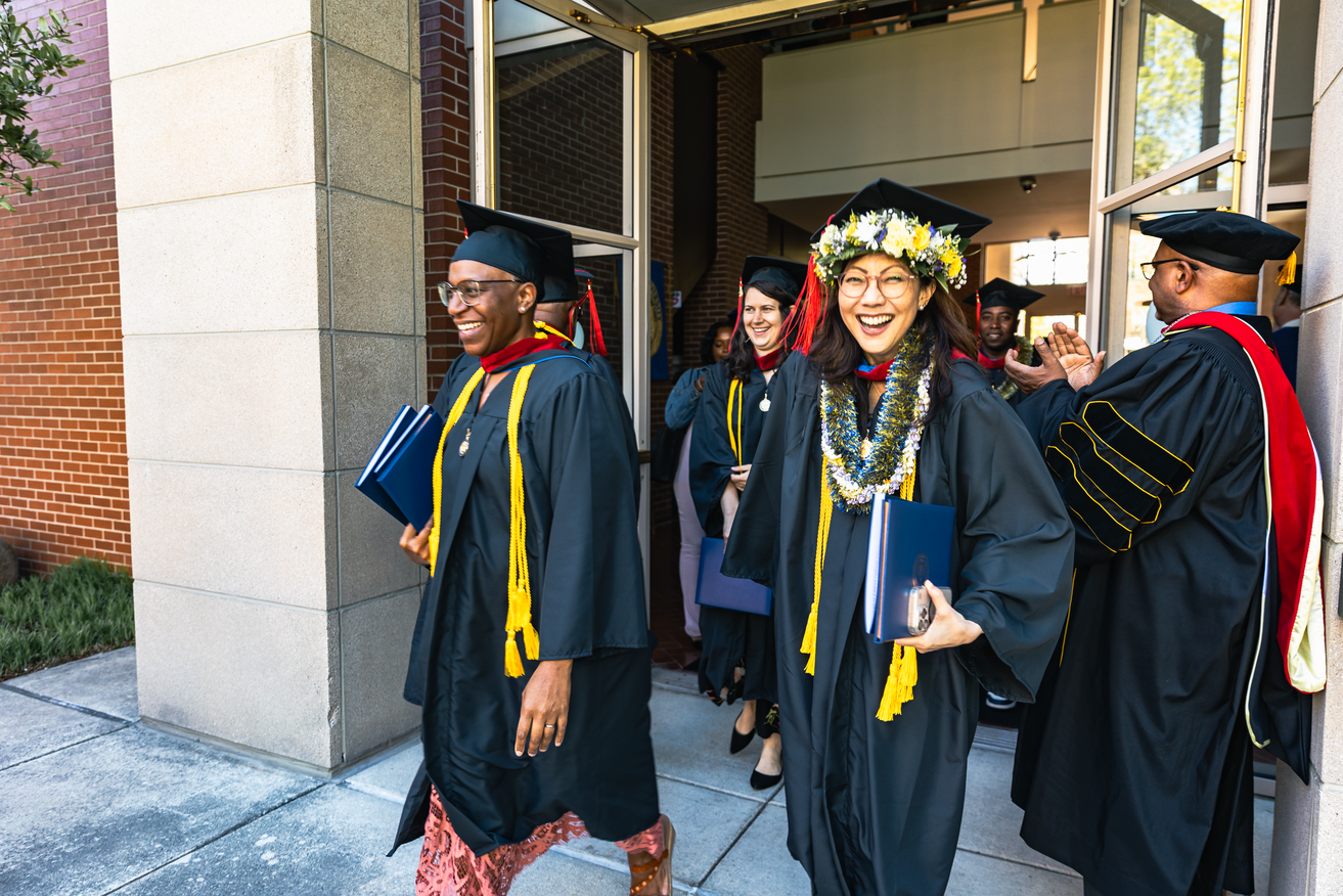Seminary master's graduate walks out of 2025 commencement with full regalia and flowers around her cap