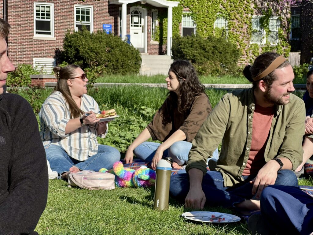 students sit on grass and enjoy meal together in the center of campus
