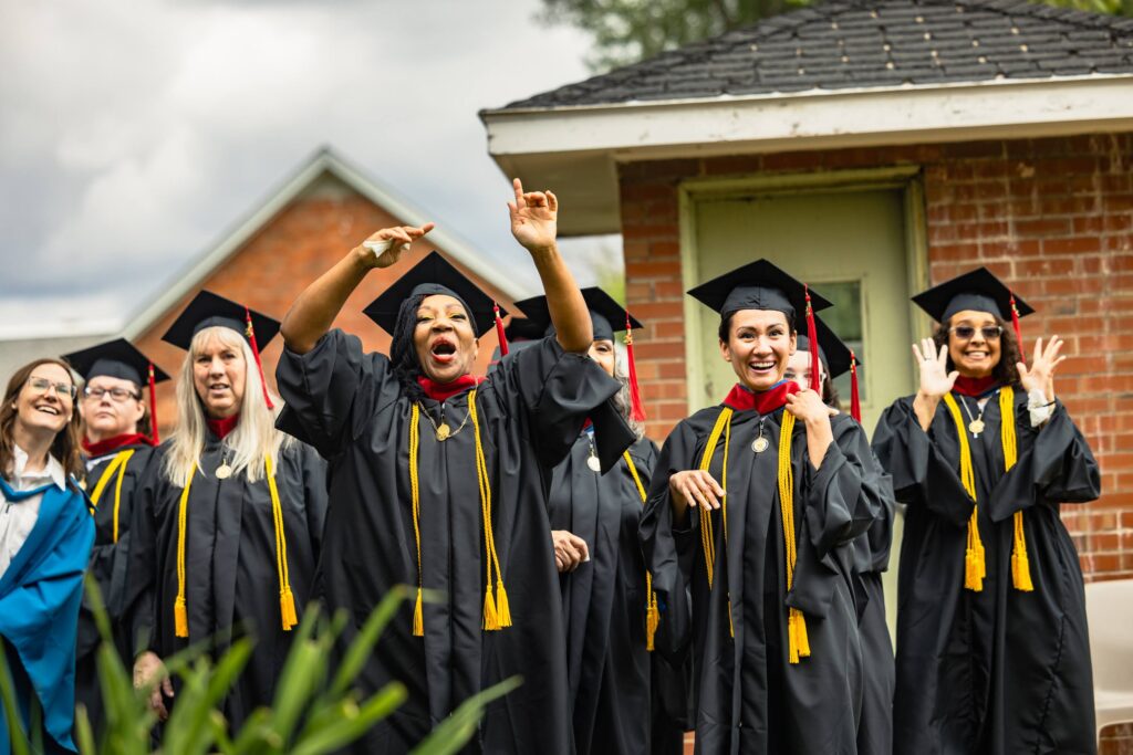 Incarcerated students wearing in black graduation robes react with surprise and big smiles