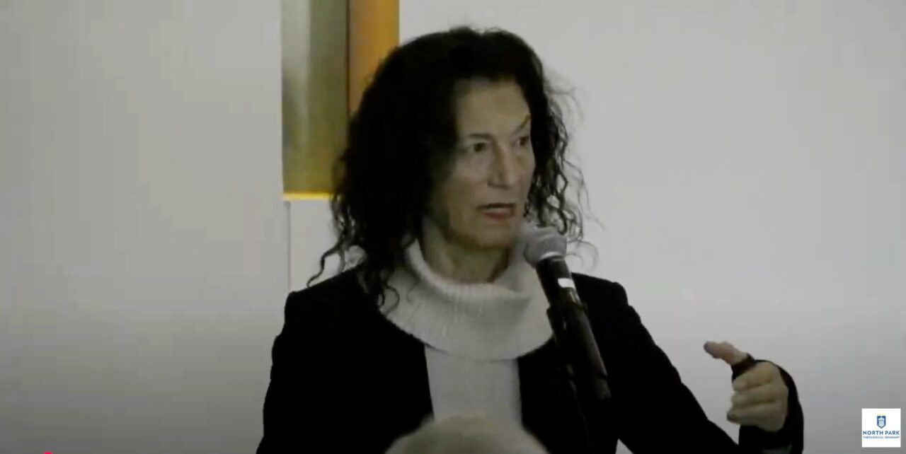 Lecturer speaks into microphone and shares a meaningful look with the audience