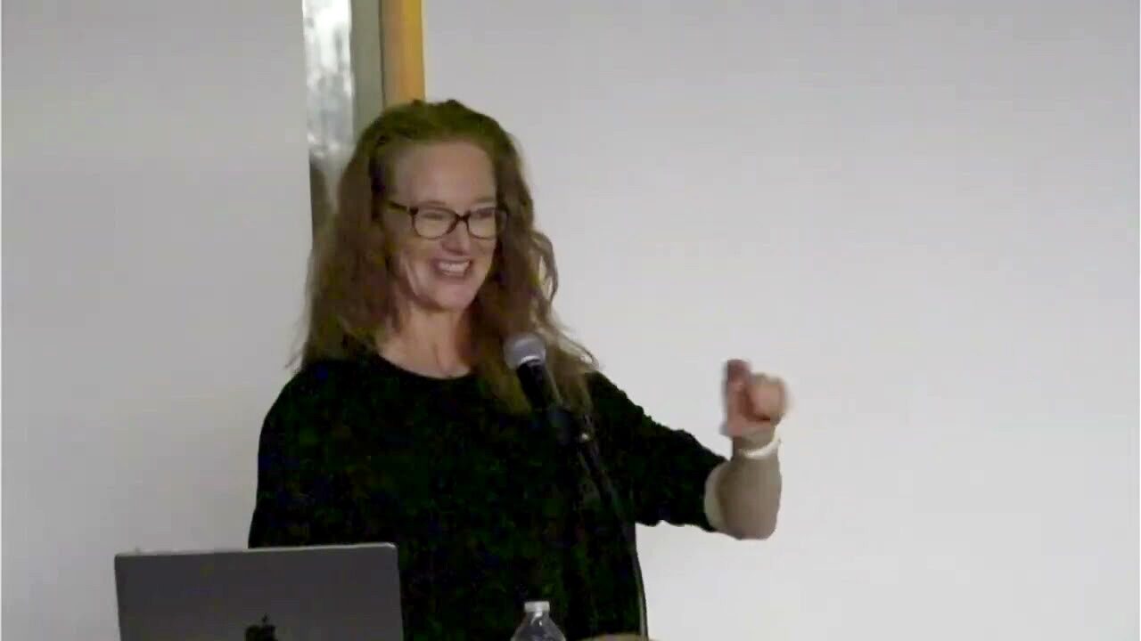 Presenter wearing glasses smiles and gestures as she lectures