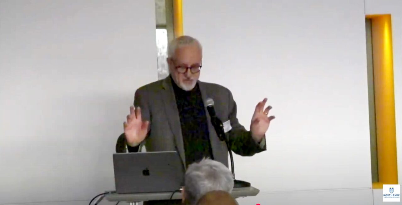 Professor gestures with his hands as he lectures at the symposium