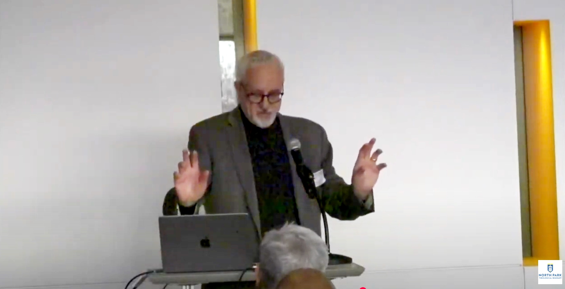 Professor gestures with his hands as he lectures at the symposium