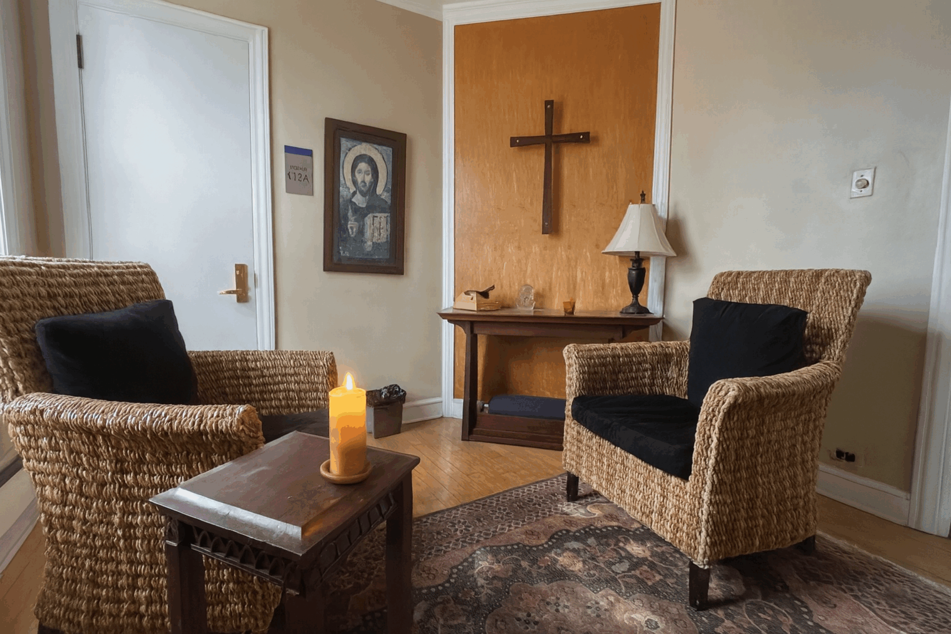 Two chairs sit empty in prayer room with lit candle and cross and image of Jesus