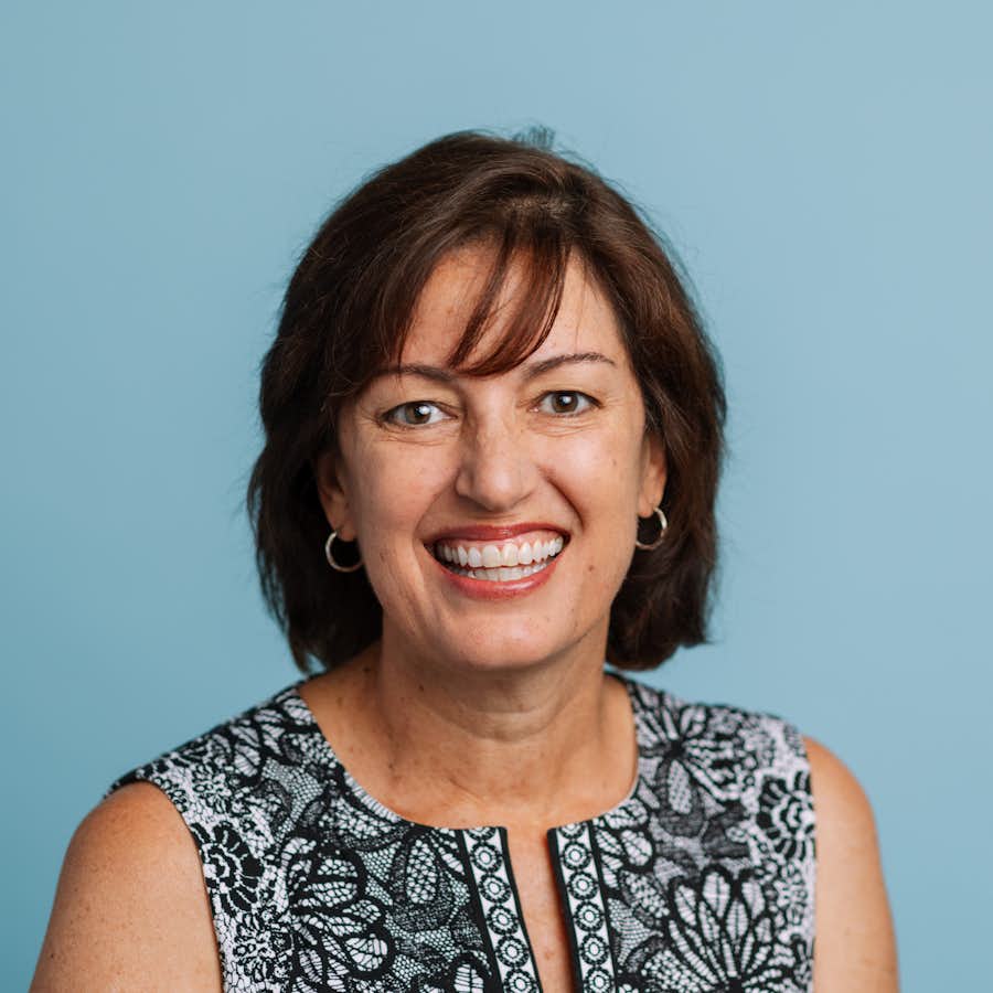 Woman with shoulder-length brown hair in printed blouse smiles at the camera