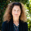 Woman with long curly hair in black blazer smiles in professional headshot