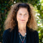 Woman with long curly hair in black blazer smiles in professional headshot