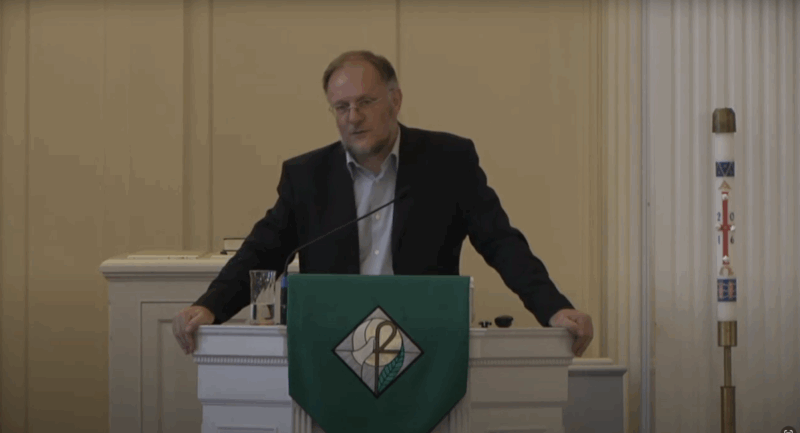 Gray-haired male professor gives presentation from behind pulpit in seminary chapel
