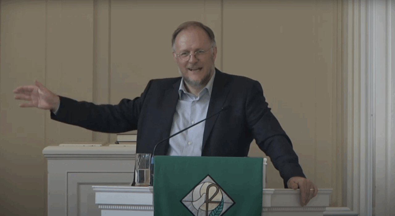 Gray-haired male lecturer presents from behind pulpit in seminary chapel