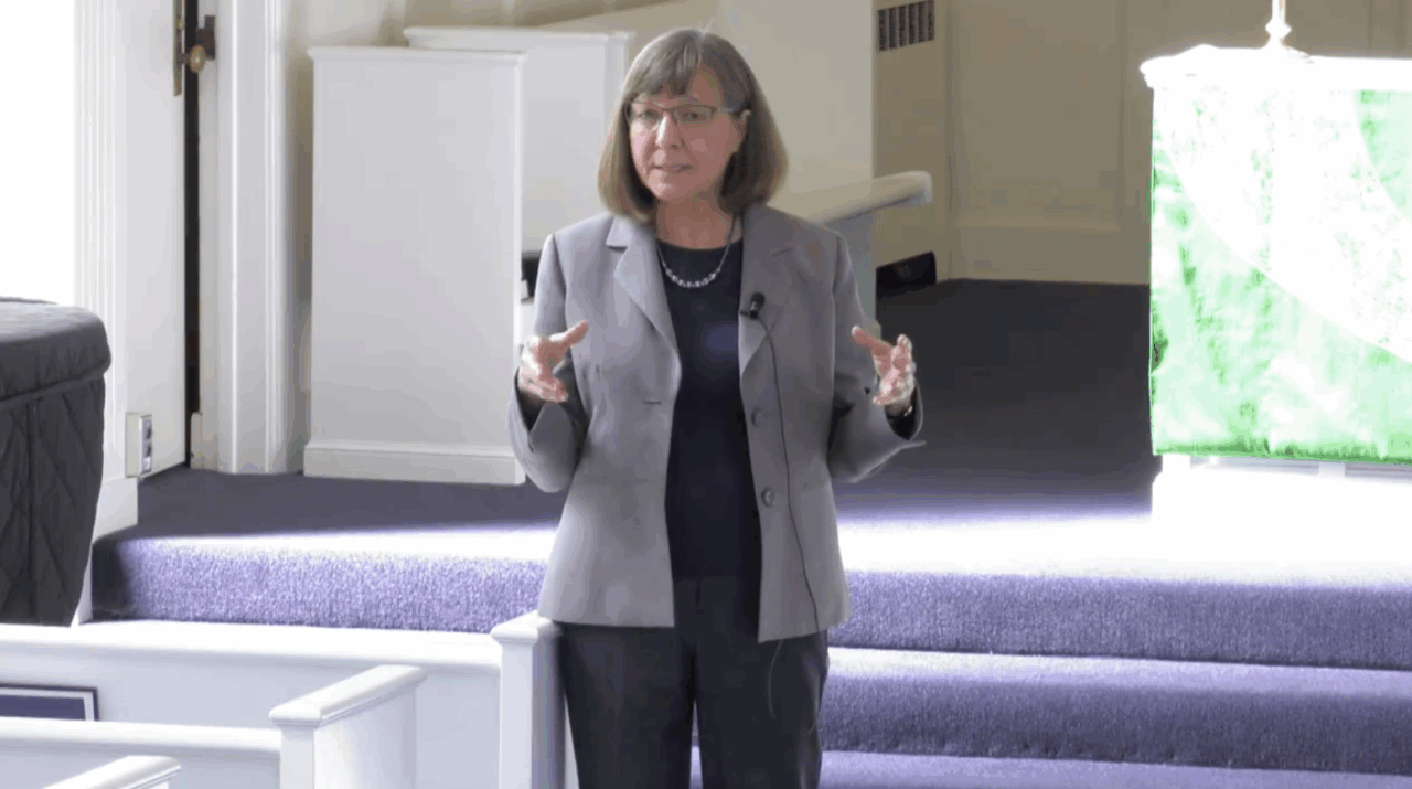 gray haired female lecturer in gray blazer responds to audience questions in the main aisle of a seminary chapel