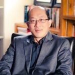 Malaysian American professor wearing glasses smiles slightly at the camera