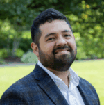 Latino man in checkered blazer smiles at the camera