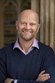 Balding bearded white man in navy sweater smiles at camera