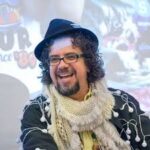 Bearded man in hat and scarf laughs in professional headshot