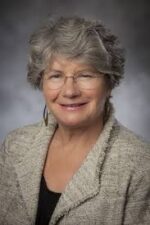 Gray-haired white woman in off-white blazer smiles at the camera