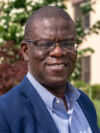 Bald black professor with glasses and navy jacket smiles at the camera