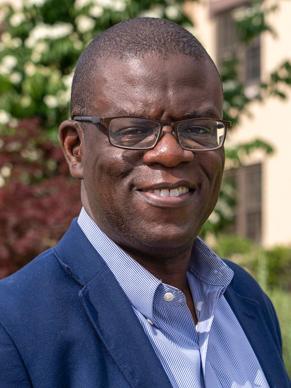 Bald black professor with glasses and navy jacket smiles at the camera