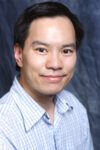 Asian-American man with blue button down shirt smiles at the camera