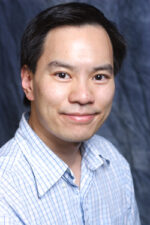 Asian-American man with blue button down shirt smiles at the camera