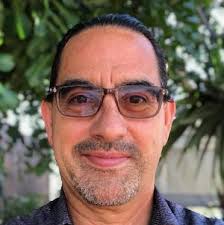 Latino man with glasses and graying beard smiles at the camera