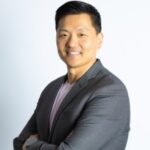 Asian man in gray blazer smiles at the camera