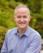 Middle aged white male professor in blue button down shirt smiles at the camera