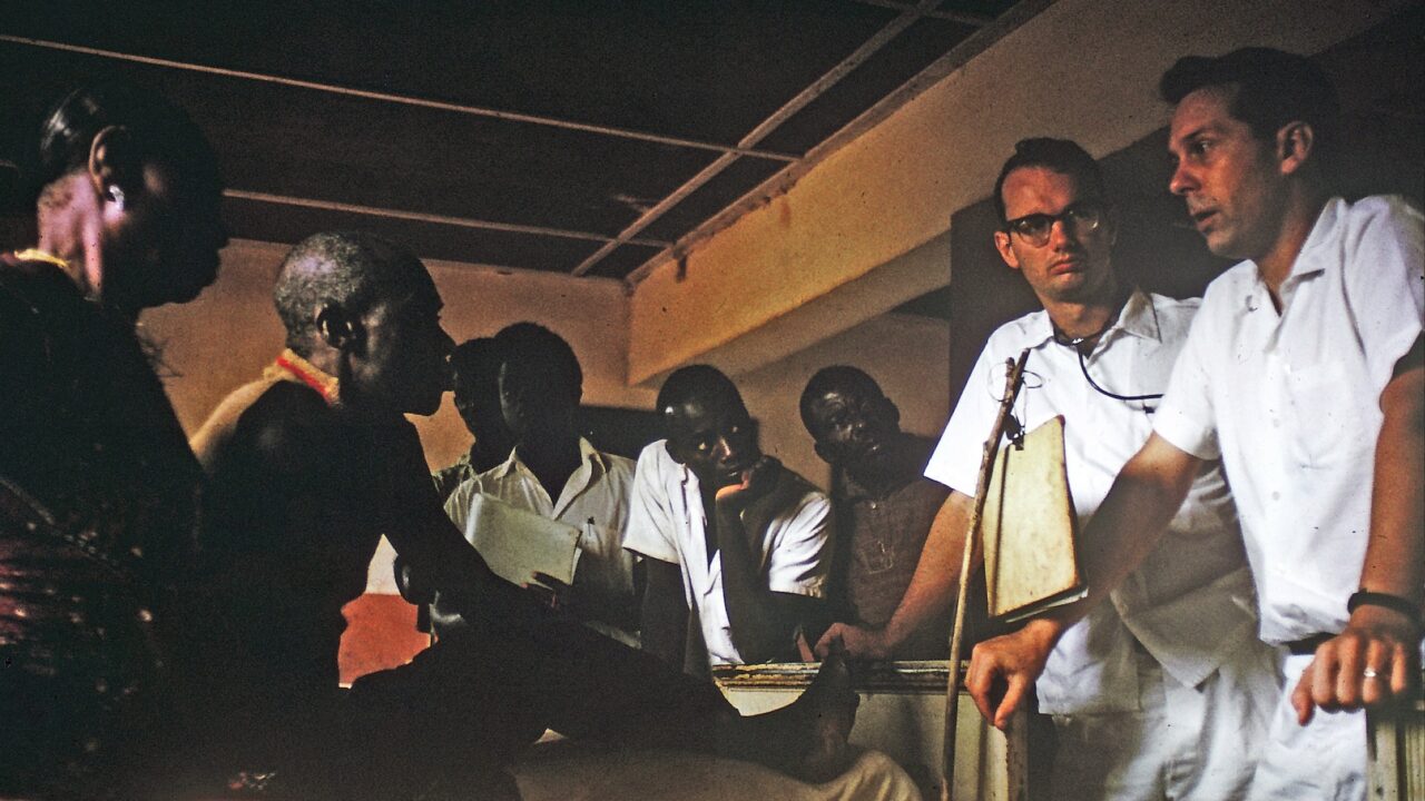 A white male doctor advises a Congolese patient and their family during hospital rounds.