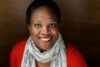 Black woman in red sweater and printed scarf smiles at the camera