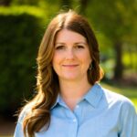 White woman with long brown hair wearing a light blue button-down shirt smiles at the camera
