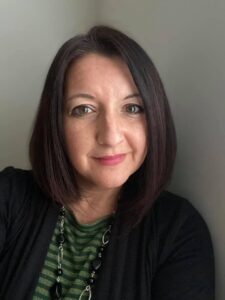 White woman with dark shoulder length hair looks at camera