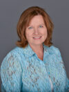 White woman with shoulder length red hair and blue lacy button up shirt smiles at the camera