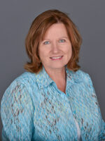 White woman with shoulder length red hair and blue lacy button up shirt smiles at the camera