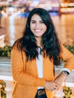 Latina woman with long hair and yellow sweater smiles at the camera