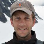 White man in gray baseball cap smiles at the camera