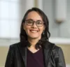 Mexican-American woman with shoulder length black hair and dark rimmed glasses smiles at at the camera