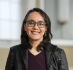 Mexican-American woman with shoulder length black hair and dark rimmed glasses smiles at at the camera