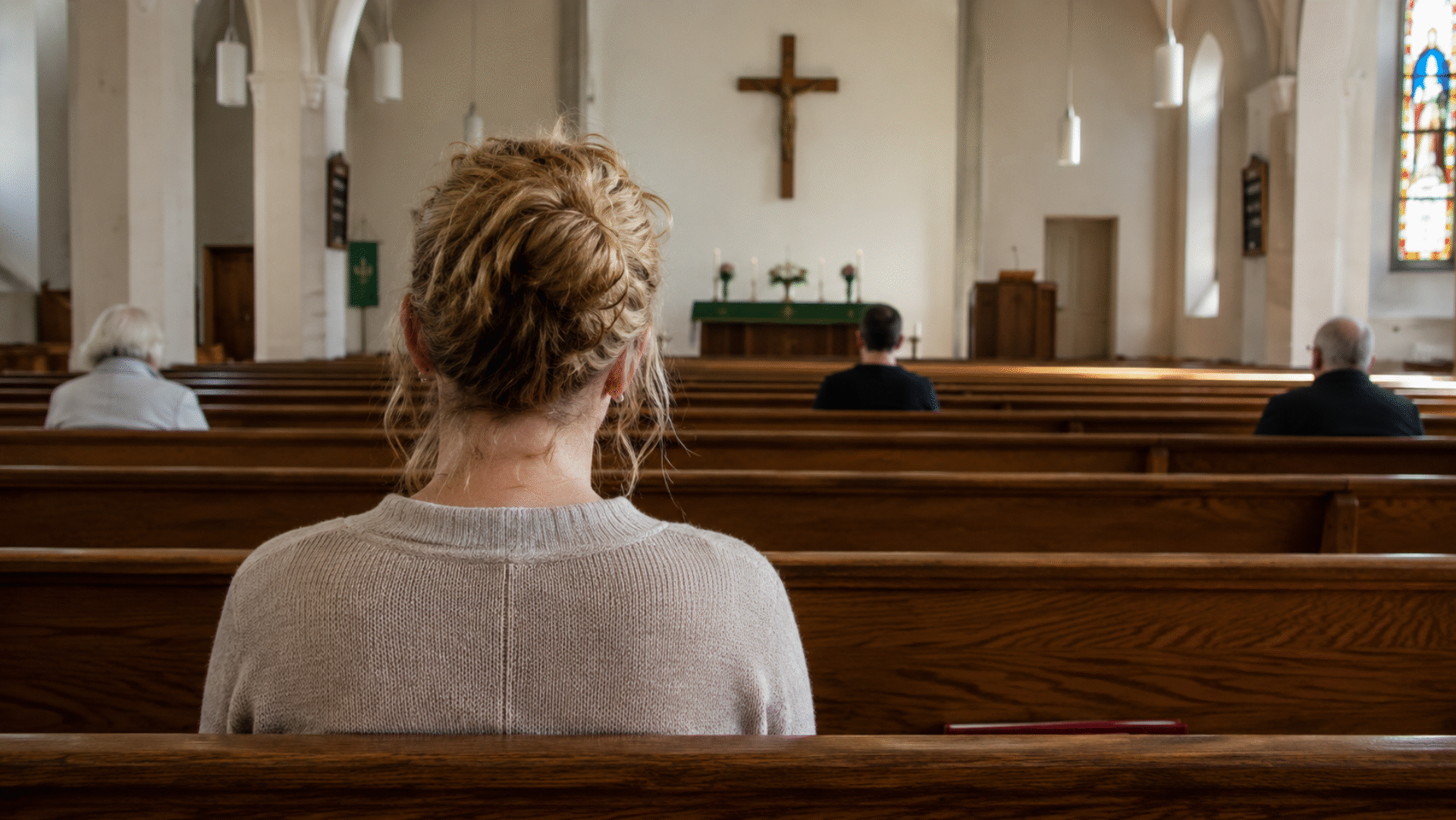 Color photograph of people sitting alone in church pews facing the altar