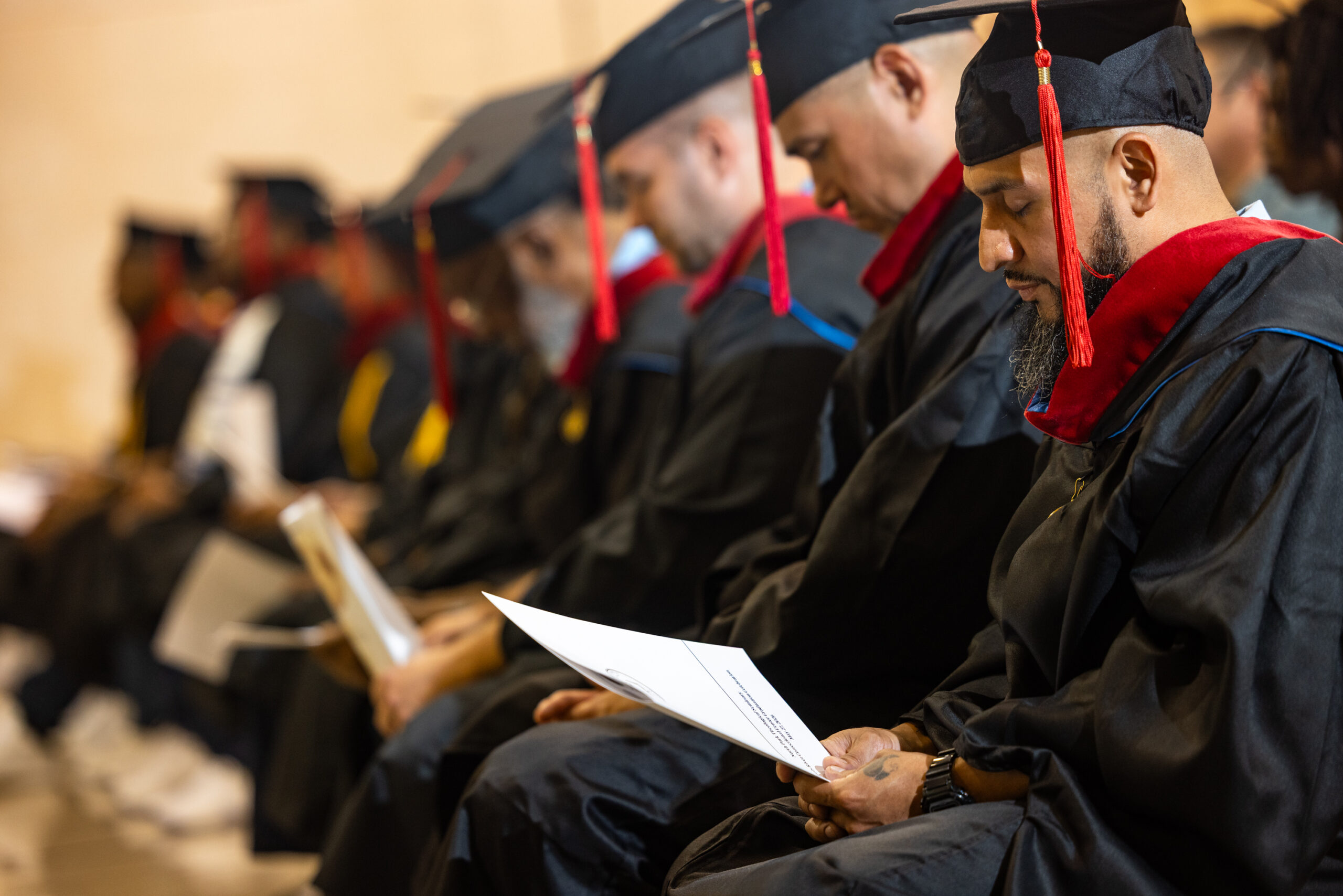 Group of male graduates bow their heads in prayer during commencement ceremony