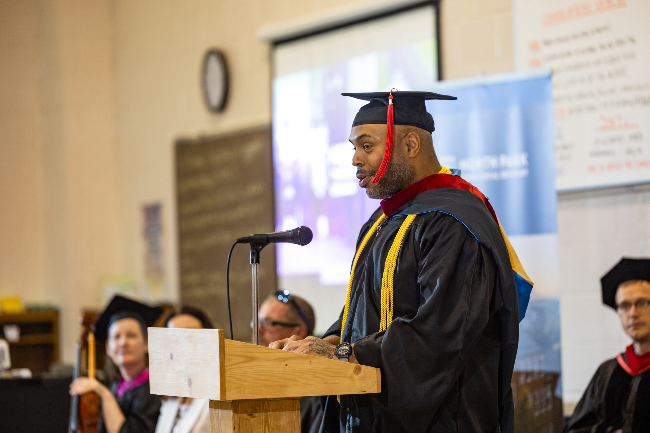 Black man in graduation regalia gives a Commencement speech