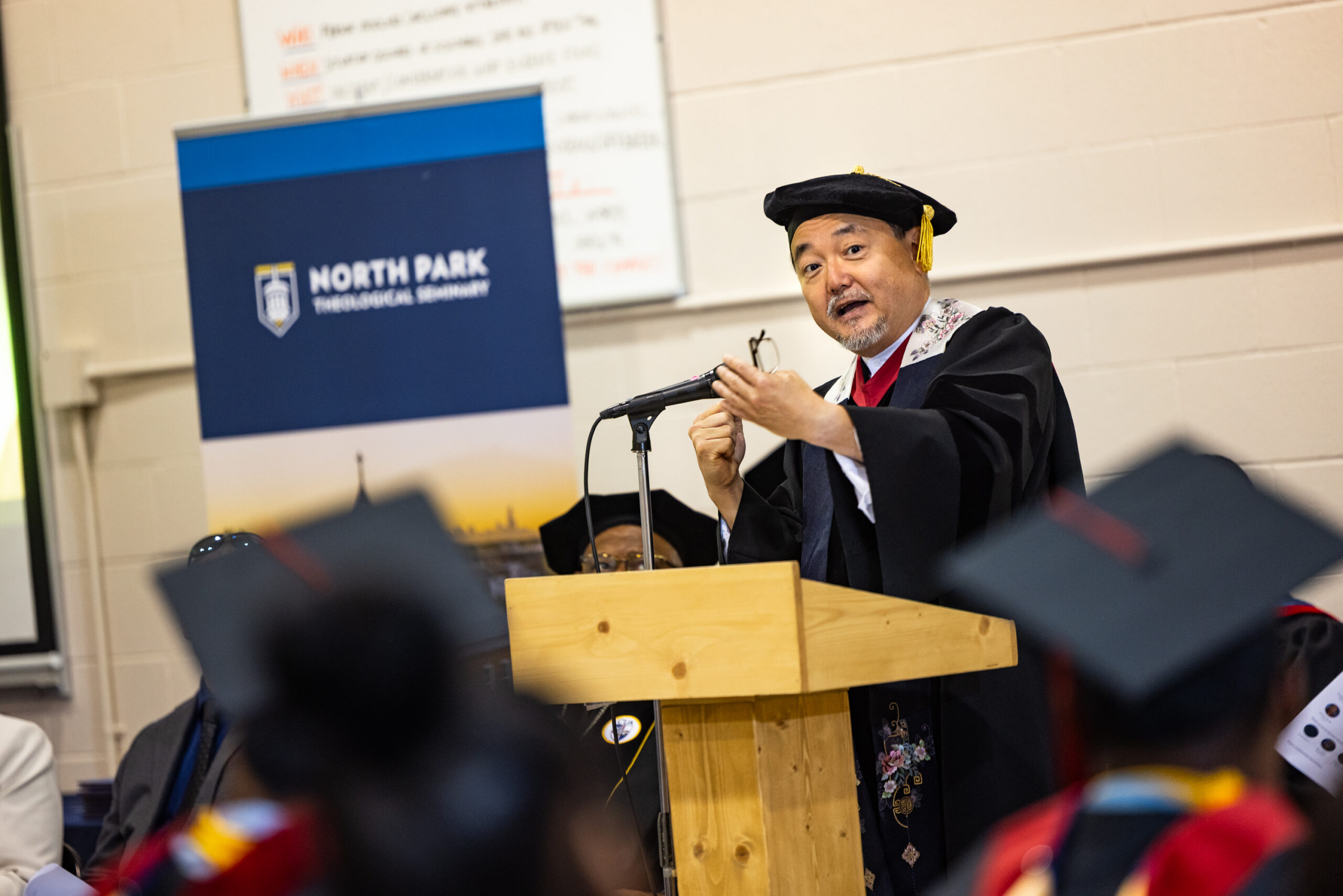 Asian American man in doctoral robes offers a speech behind a podium