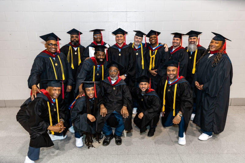 Group of male graduates in regalia smile at the camera
