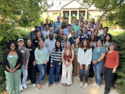 Diverse group of students stands on steps in front of brick building with white columns