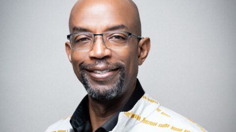 Bald Black man with goatee and glasses smiles at the camera