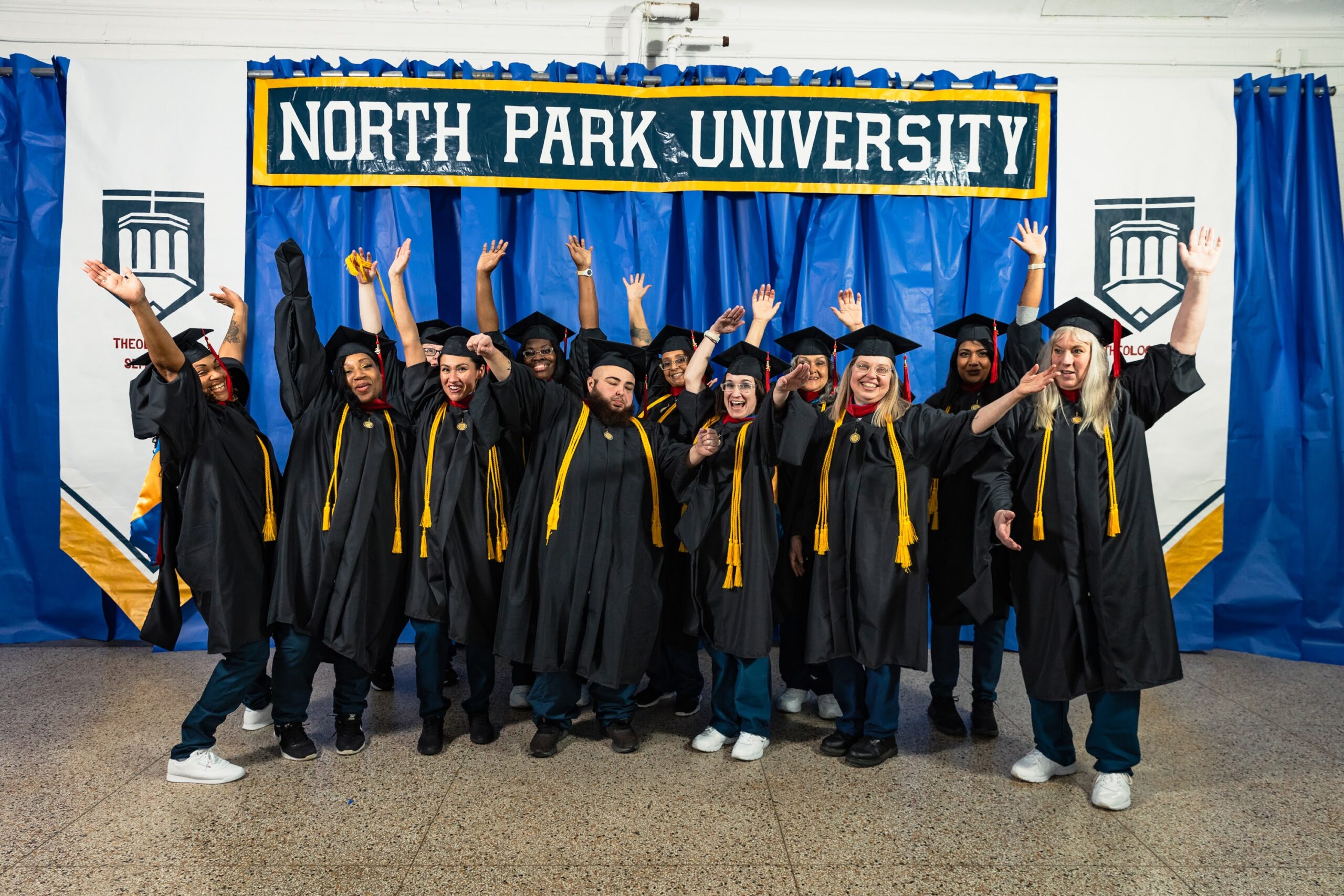 Students in academic regalia standing in front of homemade decorations in celebratory poses