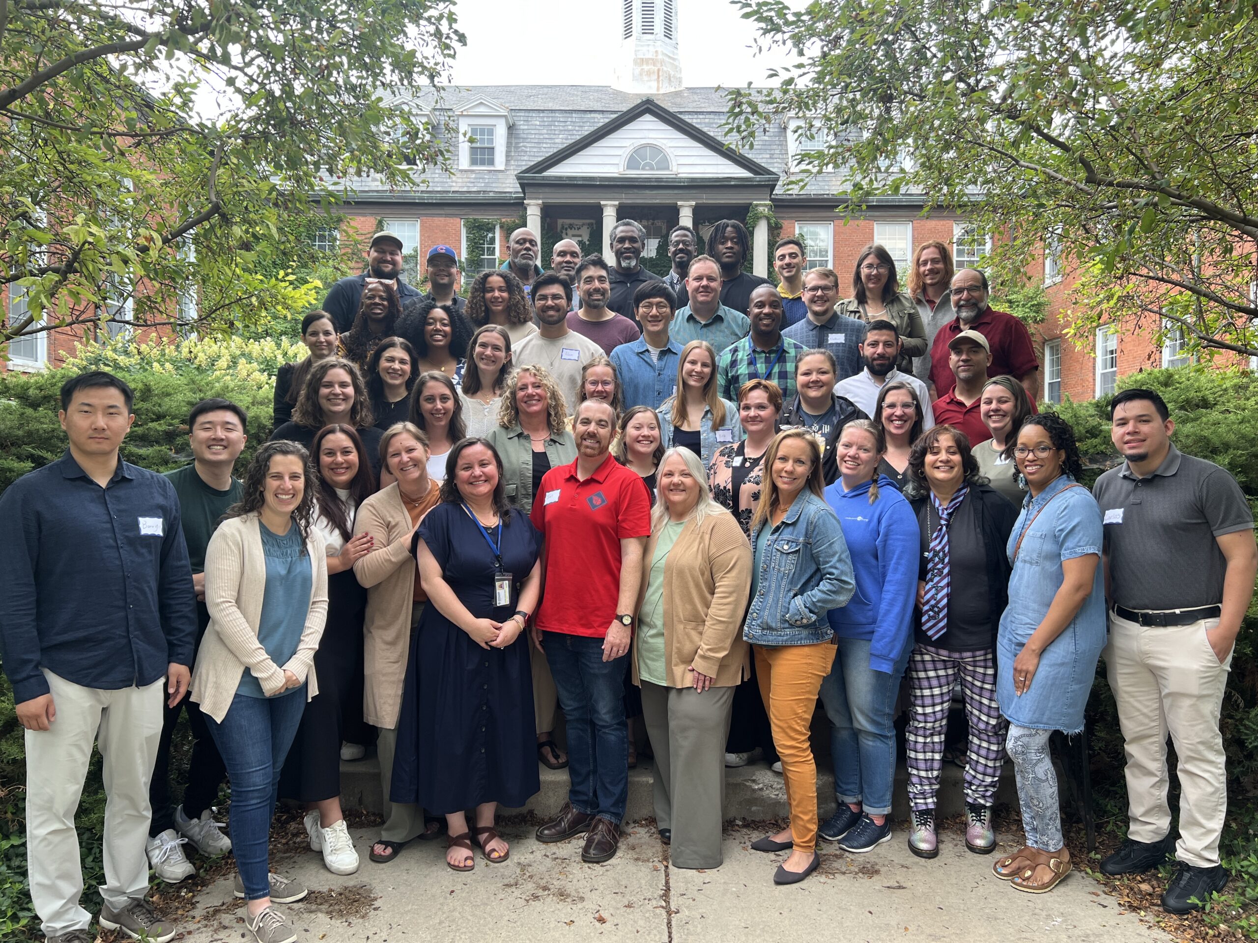 Group of diverse students stands on steps in front of brick building with white steeple